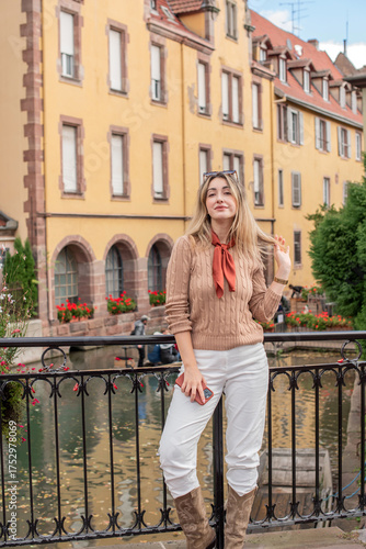 Woman wearing a beige knitted sweater, white jeans, and sunglasses, with a brown silk scarf. Casual chic outfit perfect for lifestyle, fashion on French street