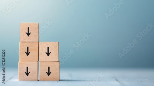 A stack of wooden blocks with downward arrows against a soft blue background, symbolizing decline or decrease.