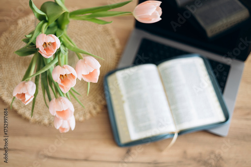 A bouquet of tulips in a vase, an open Bible and a laptop on a wooden table.