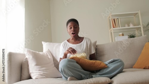 Surprised african american woman watching tv and eating popcorn
