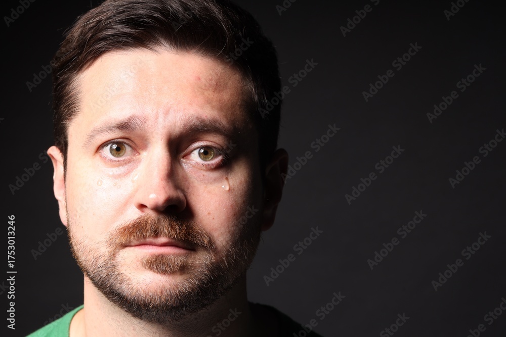 Fototapeta premium Sad man crying on black background, space for text