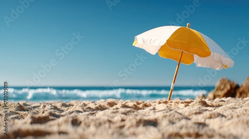 A classic beach umbrella stands alone on the sandy shore, offering shade and relaxation, showcasing the ideal summer getaway complemented by the endless blue ocean and sky.