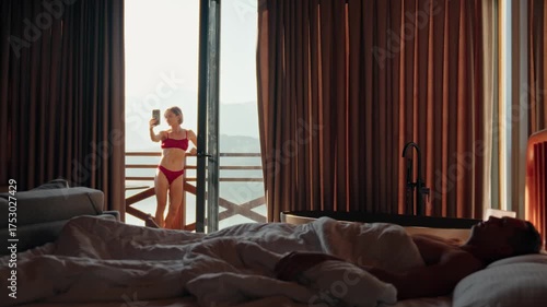 Young couple relaxing in a countryside wooden house. Woman taking a selfie on the balcony in lingerie on a sunny morning. Concept of slow life and digital presence. High quality 4k footage