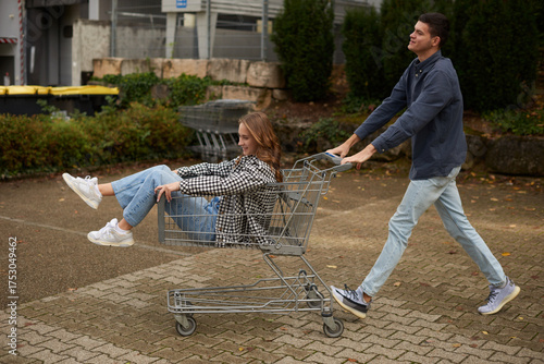 Wallpaper Mural Playful Young Couple's Shopping Cart Adventure in Vibrant Park Setting. Joyful Outdoor Moment Captures Spontaneous Love and Seasonal Casual Style. Torontodigital.ca