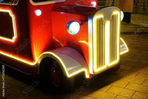 Brightly lit vintage toy car parked on a city street at night during a festive celebration