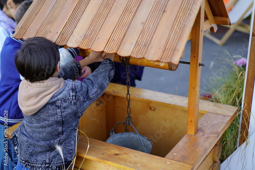 Children enjoy playing at a wooden well during a community event on a sunny afternoon in the park