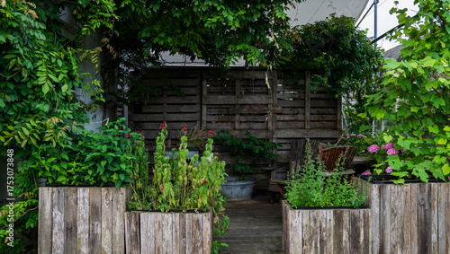 Photos Cozy garden corner with lush greenery, wooden planters filled with herbs and flowers, a rustic wooden fence, and a shaded seating area, creating a natural and tranquil outdoor retreat