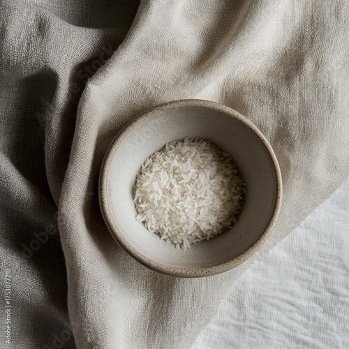 A bowl of white rice is sitting on a white cloth. The rice is spread out and not piled up
