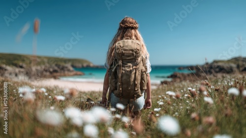 A person with a backpack stands amidst blooming wildflowers, gazing at the serene seaside landscape, embodying adventure and exploration in nature.