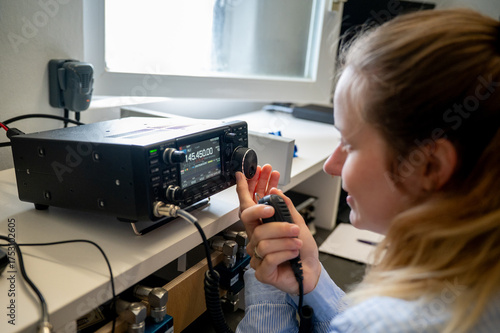 Fotografie Young woman with ribbon in her hair operating a VHF/UHF amateur radio transceive