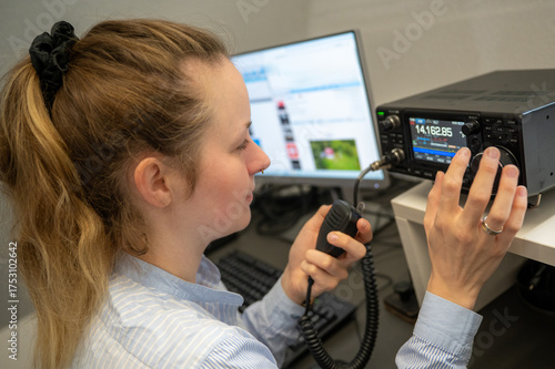 Young woman with ribbon in her hair operating amateur radio on shortwave, holding a microphone and representing YLs and females in STEM and technology fields
