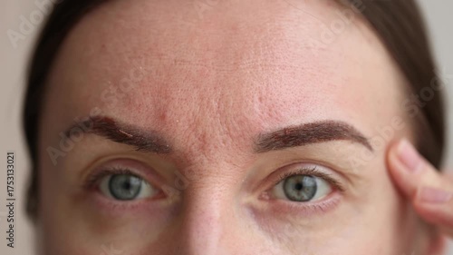 Woman looking on her healing eyebrows after permanent makeup. Closeup. 4K