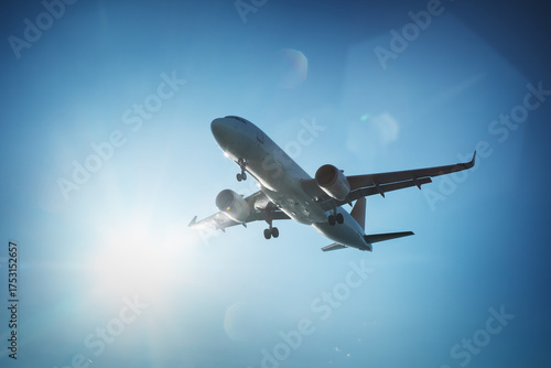 Low-angle shot of a commercial airplane in flight, captured against a clear blue sky with the sun shining brightly.
