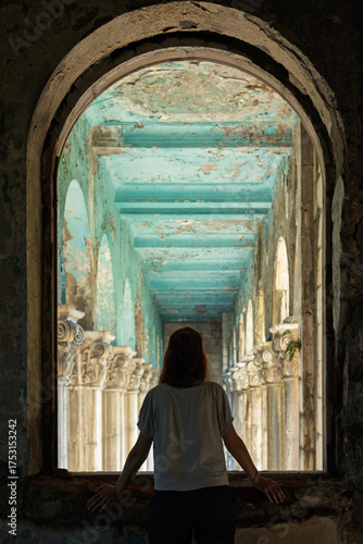 Silhouette of a woman standing at a window, looking into the decaying interior of an abandoned sanatorium in Tskaltubo, Georgia, with peeling turquoise ceilings and classical columns.
