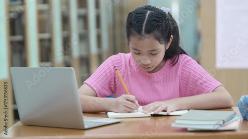 Focused girl doing homework and online learning at library using laptop. Concept of remote learning. Time management. Back to school. Education concept.