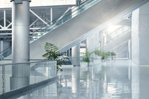 Bright, sleek, and empty corporate or public space featuring escalators, columns, and a reflective floor.