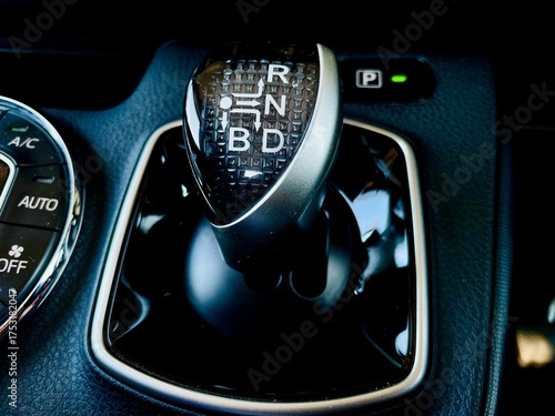 A close-up of a modern vehicle's center console featuring the circular automatic climate control panel with 'AUTO' and 'DUAL' zones, positioned next to a sleek electronic gear selector 