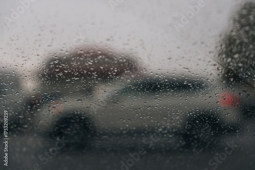 From inside a car during heavy rain. Focus is on the water droplets running down the glass. The blurred silhouettes of cars are visible through the curtain of water, depicting movement in bad weather.