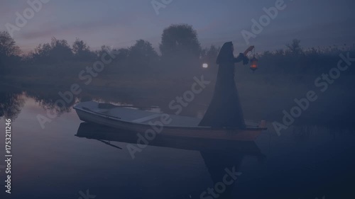 Silhouette fantasy woman witch floating in boat down river in night autumn nature fog dark trees. Mystery girl hand holding lantern with warm light. wooden ship on lake. Black dress cape hood on head