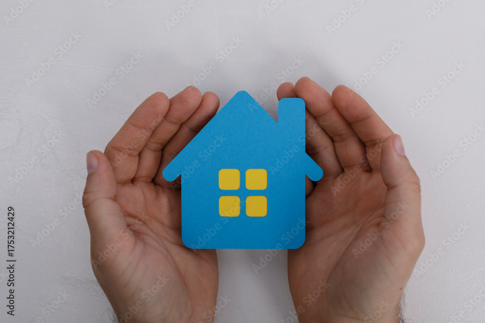 Fototapeta premium Hands gently cradling a paper house, symbolizing protection, security, and the concept of homeownership. Ideal for real estate, insurance, and s