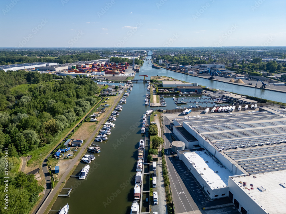 Obraz premium Klein-Willebroek, Willebroek, Antwerp, Belgium, 13th of May, 2025, A stunning aerial shot of a canal with vibrant boats, large warehouses, and lush greenery all around