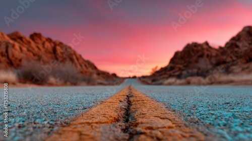 An empty road stretches towards the distant mountains, surrounded by rocky terrain and a breathtaking twilight sky that fades into soft hues, inviting adventure and exploration.