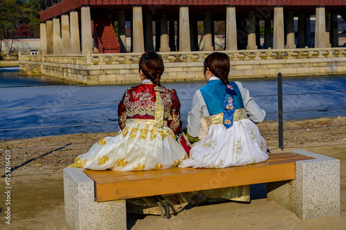 A Korean woman in traditional costume sits by a pond in a palace in winter.