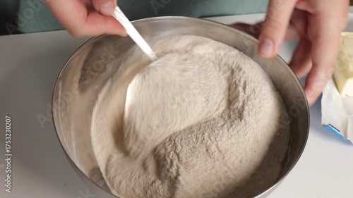 Person mixes dry ingredients in metal bowl for pie. Flour, semolina, sugar and baking powder combine. Mixing ingredients shows homemade dessert preparation.