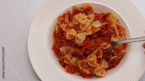 Fork scooping up bowtie pasta in thick tomato sauce, served on elegant white plate during mealtime