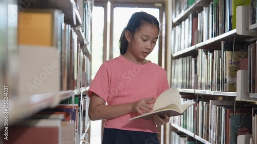 Young girl reading book in library filled with shelves, where education brings happiness and joy to every page.