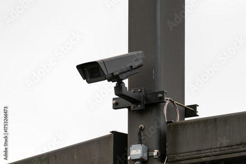 Close up on a surveillance camera on a massive mast, against a grey sky.