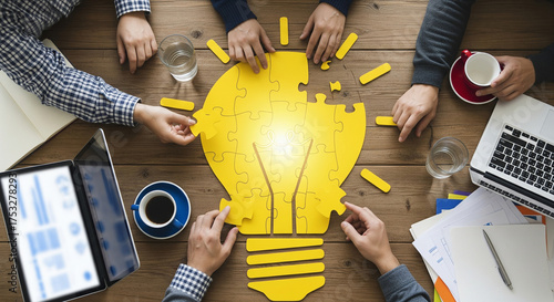 Top view of business team assembling a yellow lightbulb puzzle on a wooden table, symbolizing collaboration, innovation, and creative problemsolving