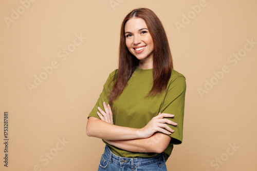 Side view young smiling happy woman wears olive green t-shirt casual clothes hold hands crossed folded look camera isolated on plain pastel light beige background studio portrait. Lifestyle concept.