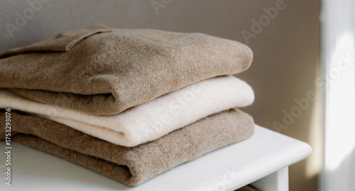 Three thin warm sweaters on a white closet shelf.