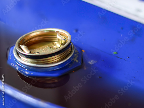 Close-up of the open bung hole and brass plug of a blue industrial drum filled with dark liquid, likely oil or lubricant.