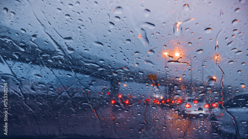 Atmospheric view of a rainy highway at dusk with water on the windshield and blurred taillights