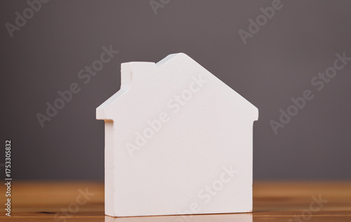 A white wooden model house sits on a wooden surface against a neutral background, ideal for real estate and homeownership concepts.