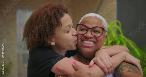 Affectionate embrace between teen son and mother, boy kissing her cheek while hugging outdoors, heartfelt bond, intergenerational connection, family love