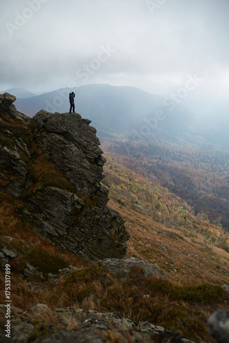 Hiker stands on rocky outcrop overlooking misty mountain landscape in autumn. Autumn hiking in Carpathian Mountains, Ukraine
