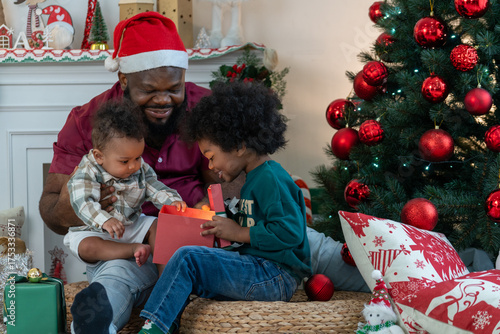 Happy African American dad with two son children celebrating Christmas. Black father and kids opening Christmas gifts.