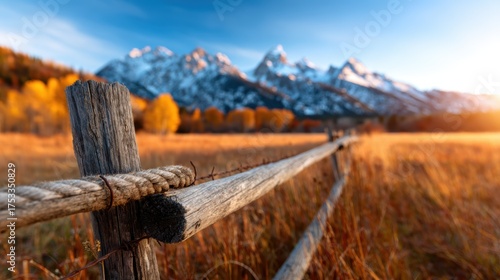 A beautiful rustic wooden fence in the foreground showcases the grandeur of snow-capped mountains, surrounded by vibrant autumn foliage capturing nature's serenity.