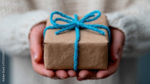 A beautifully wrapped gift box with a striking blue ribbon is held lovingly in hands, symbolizing anticipation and joy of giving and receiving gifts during special occasions.
