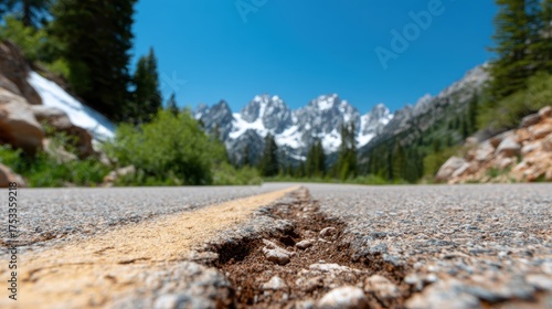 A close-up view of an asphalt road cracked with age, leading towards majestic snow-capped mountains, depicting nature's beauty and the passage of time.