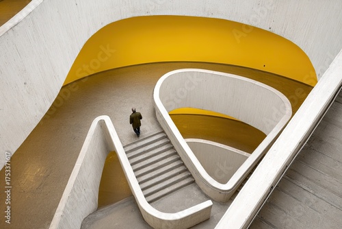 Elevated perspective of a person walking down a curved staircase with yellow and white walls