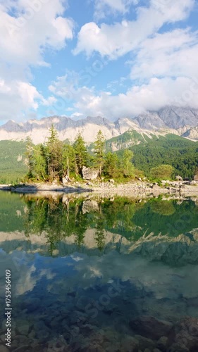 Eibsee Lake, Mountain Slopes with Forest, Island and Zugspitze Massif on Sunny Day. Ripple and Reflection on Water. Bavaria, Germany. Vertical Video