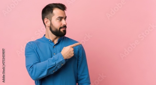Man with beard pointing to the side on a pink background.