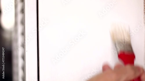 A man paints an old cabinet with a brush. He holds a red brush in his hand against the background of an old white cabinet.