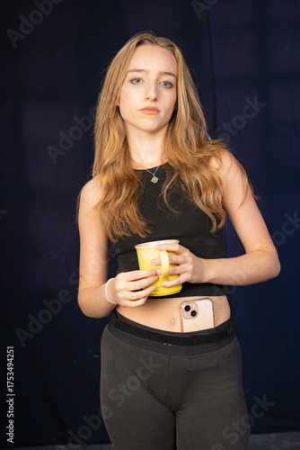 A young woman poses with a casual outfit and a yellow mug, her confident expression complemented by a dark background, creating a striking artistic portrayal.