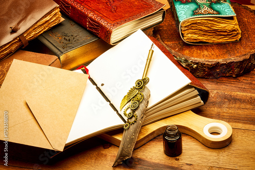 A creative artistic still life composition featuring multiple vintage journals, an open blank notebook, a decorative steampunk feather pen, kraft paper envelope, and an ink bottle 
