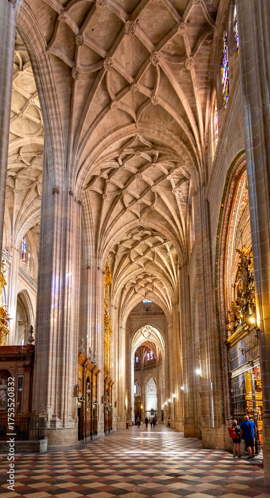 Fototapeta premium The Segovia Cathedral interior showcases towering Gothic arches and an ornate vaulted ceiling. Massive columns frame the central altarpiece and detailed stained glass